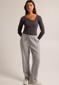Pantalon de survêtement gris avec une taille à cordon de serrage, associé à un haut à manches longues ajusté de couleur gris foncé avec un décolleté en V. Texture lisse.