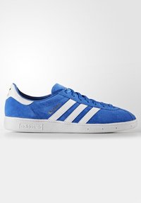 Blå mockasinsneaker med vita tre ränder, gummisulor och guldfärgad logotyp. Har runda skosnören och vadderad krage för komfort.