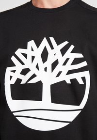 Felpa nera con un grande logo geometrico bianco a forma di albero al centro. Collo a giro e texture morbida. Design grafico distintivo.