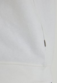 White cotton sweatshirt featuring a textured surface, a fitted hem, and a small brand tag on the side. Simple and minimalistic design.