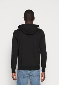 Felpa nera con cappuccio regolabile da coulisse, polsini e orlo a coste. Presenta il logo "TOM TAILOR" sul retro, realizzata in un tessuto morbido e strutturato.