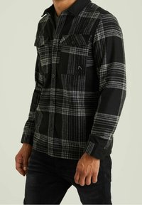Černá a šedá kostkovaná flanelová košile s dlouhými rukávy, zapínáním na knoflíky vpředu a dvěma náprsními kapsami. Obsahuje texturovanou látku a kontrastní límec.