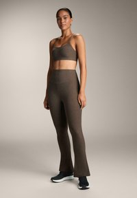 Barna sportmelltartó és illeszkedő, magas derékú leggings, amelynek alja enyhén bővül. Az anyag lágy megjelenésű, finom textúrával. Fekete edzőcipővel kiegészítve.