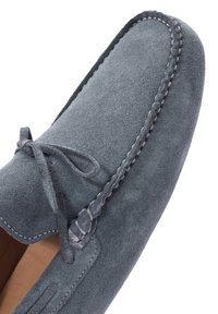 Grijze suède moccasin schoen met een gestructureerde bovenkant, ronde neus en een decoratieve gevlochten rand langs de zijkant. Dunne veters geknoopt aan de bovenkant.