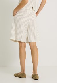 Shorts blancs rayés avec poches latérales, s'arrêtant juste au-dessus du genou. Associés à des ballerines marron décoratives avec des accents circulaires.