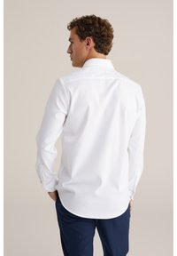 Balti marškiniai ilgomis rankovėmis, užsegami sagomis, su išlenktu apatine kraštine, minkšta tekstūra ir klasikiniu apykakle. Turi sagomis užsegamus rankogalius ir minimalistinius dizaino elementus.