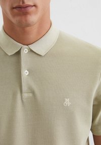 Licht olijfgroen poloshirt met een textuurstof, een klassieke kraag en twee knopen, met een subtiel geborduurd logo op de borst.
