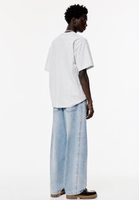 Tricou gri cu mânecă scurtă și un croi lejer, asortat cu blugi largi de culoare albastru deschis și bocanci cu talpă groasă de culoare maronie. Design simplu, fără modele.