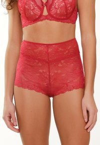 Stringhi rossi in pizzo a vita alta con intricati motivi floreali e bordi ondulati. Texture morbida con una cintura liscia per il massimo comfort.