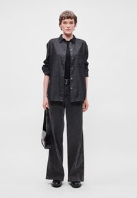 Μαύρο τζιν πουκάμισο με κουμπιά μπροστά, σε συνδυασμό με φαρδιά μαύρα τζιν. Περιλαμβάνει μια μαύρη τσάντα και χοντρές μαύρες παπούτσια.