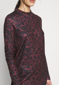 Långärmad topp i vinröd med svart leopardmönster. Tillverkad av texturerad tyg med rund halsringning och subtila sömdetaljer.