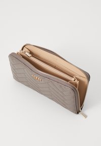 Cartera gris acolchada con cierre de cremallera, que cuenta con un interior beige, compartimentos para tarjetas y un pequeño compartimento con cremallera. Acento en hardware en tono dorado.
