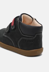 Stivaletto in suede nero con accenti rossi, cuciture bianche e suola in gomma marrone. Presenta un collare imbottito per il comfort. Logo Geox visibile.