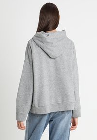 Felpa grigia over-size con cappuccio realizzata in un tessuto morbido, caratterizzata da una vestibilità rilassata con maniche ampie e un orlo a costine.