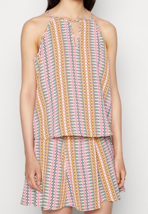 Femme portant une robe sans manches à col halter avec un motif zigzag coloré en rose, jaune, bleu et blanc, debout, bras détendus.