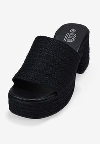 Sandalias de plataforma abiertas en la parte delantera de color negro con textura trenzada, un tacón grueso y una plantilla suave similar al cuero. Presenta una amplia cinta superior y una base sólida.