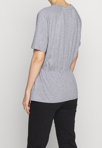 Top corto gris de manga corta con un ajuste holgado y detalle fruncido en la cintura, hecho de una tela suave. Pantalones negros completan el atuendo.