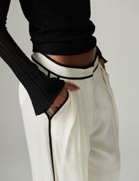 Άτομο που φοράει λευκό παντελόνι ψηλής μέσης με μαύρο περιθώριο και μαύρο ριμπ μακρυμάνικο τοπ, με τα χέρια κρυμμένα στις τσέπες του παντελονιού.