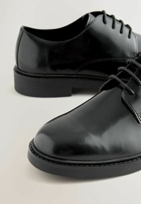 Schwarze Lederschuhe mit glänzender Oberfläche, runder Spitze, dünnen Schnürsenkeln und einer robusten Gummisohle. Minimalistisches Design ohne zusätzliche Muster.