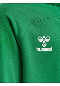 Grön sporttröja gjord av strukturerad tyg, med ett prickigt mönster på ena sidan och en vit "hummel"-logotyp framtill.