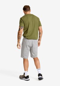 Olivgrön t-shirt med kort ärm och grå shorts. Shortsen har resårmidja och en bakficka. Idrottsskor med svarta och grå accenter.