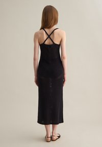 Abito nero lavorato a maglia con corpino aderente e spalline incrociate sul retro. Presenta una lunga gonna fluente e un motivo testurizzato su tutta la superficie.