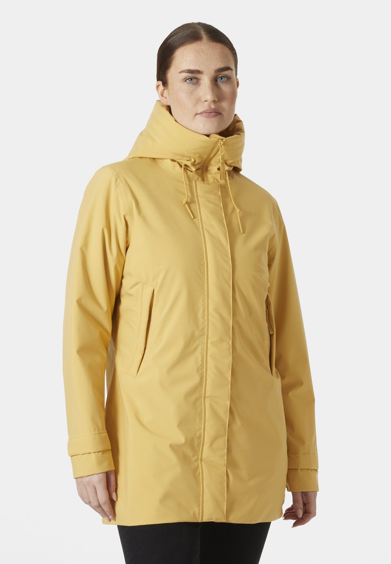 Chaqueta impermeable amarilla con un alto cuello y capucha ajustable. Presenta bolsillos laterales y un acabado suave y texturizado.