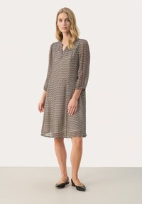 Sheer, knee-length dress with a zigzag pattern in brown and cream shades. Features a V-neck and three-quarter sleeves, paired with black flats.