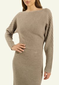 Strickkleid in Beige, mit gerippter Textur, weitem U-Boot-Ausschnitt und langen Ärmeln. Geschmeidiges, enganliegendes Design, das sich an der Taille verjüngt.