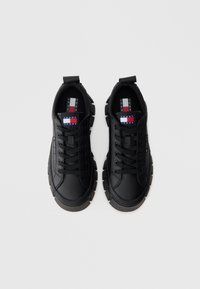 Schwarze Sneaker mit abgerundetem Zeh, strukturierter Synthetik-Oberfläche, dicker Gummisohle und flachen Schnürsenkeln. Verfügt über ein Logoschild mit rot-weiß-blauen Akzenten.