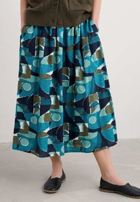 Kék és zöld mintás szoknya geometriai formákkal, rugalmas derékkal és zsebekkel. Fekete slip-on cipőkkel párosítva.