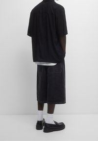 Maglietta nera a maniche corte, vestibilità comoda, abbinata a pantaloni shorts scuri fino al ginocchio, calze bianche e scarpe nere chunky. Design semplice, look casual.