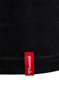 Schwarzer Stoff mit einem gesteppten Saum und einem kleinen roten Etikett mit dem weißen „hummel“-Logo und Bienen-Symbol.
