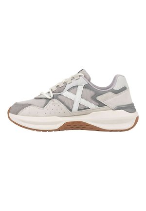 Zapatilla deportiva gris claro y blanca con paneles de malla y ante, cordones blancos, suela blanca gruesa y suela exterior marrón texturizada, vista lateral.