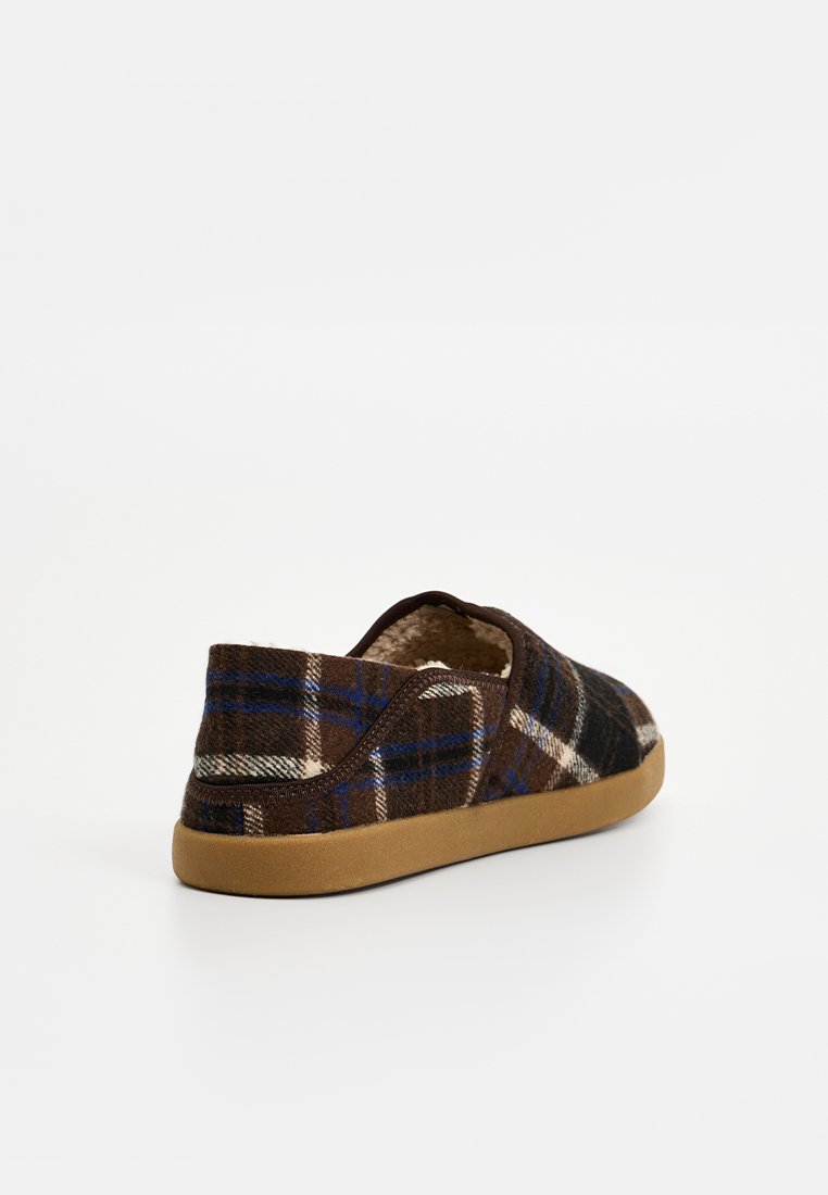 Zapatillas de lana en cuadro marrón con detalles en azul y blanco, que cuentan con un upper texturizado y una suela de goma marrón. Forro suave visible.
