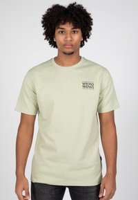 Světlounce zelené bavlněné tričko s krátkými rukávy a kulatým výstřihem; na levém prsu má černý grafický potisk.