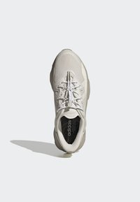 Baskets de sport gris clair avec une tige texturée, un col rembourré et des lacets blancs. La semelle intérieure présente un motif en vagues noir.