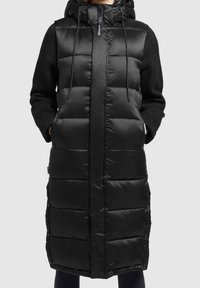 Czarna, długa kamizelka puchowa z kapturem i teksturowanymi czarnymi rękawami. Posiada zamek błyskawiczny i zapięcie na guziki, z poziomym pikowaniem.