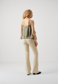 Olive green, sleeveless top with ruffled hem, paired with fitted beige flared pants. Black heeled boots complete the outfit.