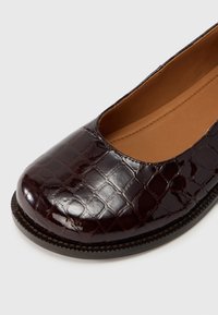 Μπαλαρίνα από βουργουνδί δέρμα πατέντας με υφή κροκοδειλίου, στρογγυλή μύτη και ελαφρύ πέλμα με διακριτικές ραφές.