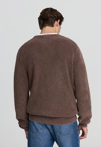 Maglione marrone a coste con una vestibilità ampia e maniche lunghe, caratterizzato da un tessuto testurizzato e un colletto rotondo, indossato con jeans blu.