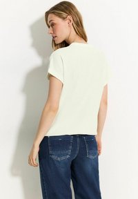 Ljusgul texturerad topp med korta ärmar, i kombination med mörkblå jeans. Toppens design har en rund halsringning och en avslappnad passform.