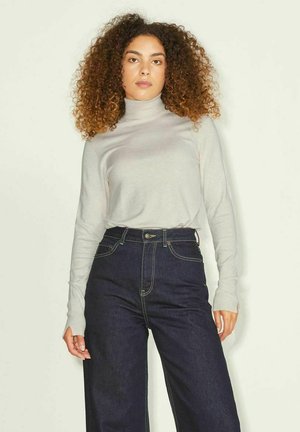 Camisa de cuello alto gris claro, de manga larga; combinada con unos pantalones vaqueros oscuros de denim de pierna ancha y cintura alta, con costuras amarillas y bolsillos frontales.