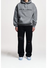 Gray hooded sweatshirt with "2Y STUDIOS" printed in black. Paired with black distressed jeans and blue sneakers. Simple, casual design.