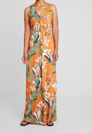 Robe maxi orange sans manches avec un imprimé floral blanc et vert et un détail de nœud torsadé sur la poitrine, portée avec des sandales noires.