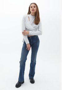 Ljusgrå långärmad topp med asymmetrisk utskärning, i kombination med mörkblå utsvängda jeans och svarta klumpiga stövlar.