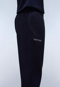 Navy blue sweatpants featuring a smooth texture, elastic waistband, and side pocket, with "Napapijri Geographic Since 1987" printed in white.