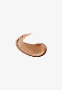 Kremet foundation-test i en varm karamellfarge. Glatt tekstur med lett glans, med fine penselstrøk mønstre i kantene.