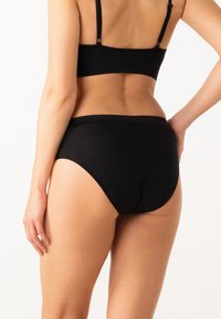 Sous-vêtements en coton noir avec une texture douce, une taille haute et une délicate bordure en dentelle le long du bord supérieur.