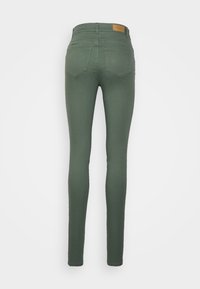 Vaqueros ajustados de mezclilla verde con una cinturilla de media altura, dos bolsillos traseros y una etiqueta de logo de cuero en la cintura. Textura suave.